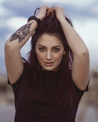 Portrait of young woman with arms raised standing outdoors