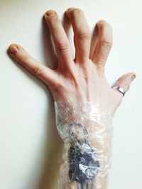 Cropped hand of man with tattoo against white wall