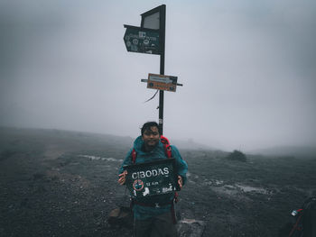 Man standing on road sign against sky