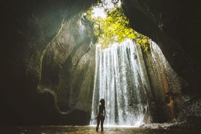 Woman standing in river against waterfall