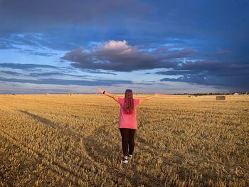 Woman with pink blouse and long hair standing on a wheat field and looking at the cloudy sky