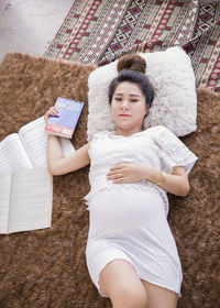 High angle portrait of woman reading books while lying on rug at home