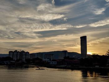 Buildings by sea against sky during sunset