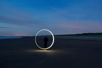 Man spinning wire wool at sandy beach against sky during dusk