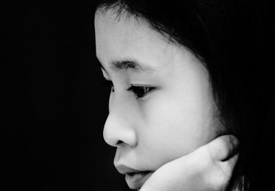 Close-up portrait of girl looking away against black background