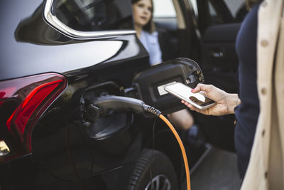 Portrait of mother, father and two daughters standing by car at electric vehicle charging station