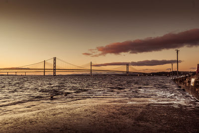 View of suspension bridge over river at sunset