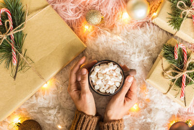 High angle view of woman holding cup of cocoa with marshmallow 