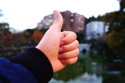 Cropped hand gesturing thumbs up sign in city