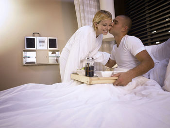 Man kissing girlfriend on bed in hotel room