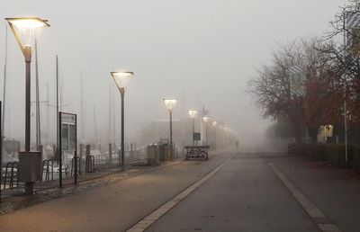 Illuminated street lights in foggy weather against sky