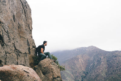 Young man on rock against sky