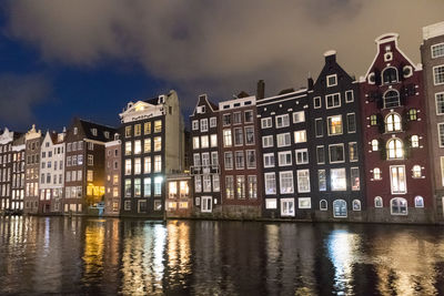 Buildings by river against sky at dusk