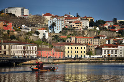 Boats in river by buildings in town against sky