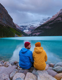 Rear view of man sitting on rock by lake