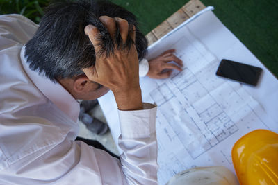 High angle view of architect with hand in hair looking at blueprint on table