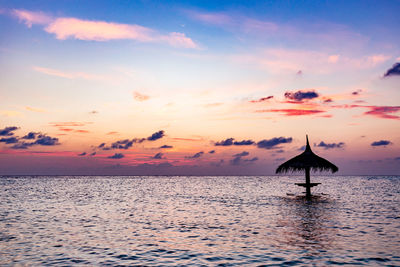 Thatched roof in sea against sky during sunset