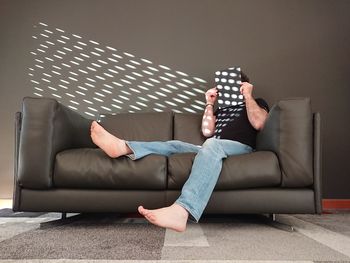 Full length of man hiding face while sitting on sofa at home