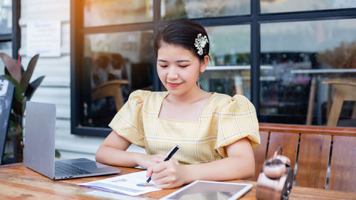 Young woman using mobile phone while sitting on table