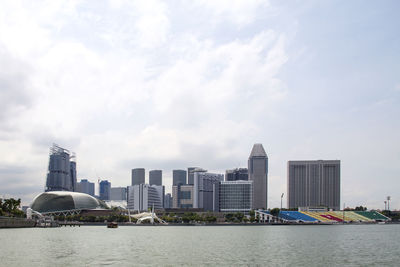 Sea by modern buildings against cloudy sky