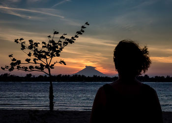 Rear view of silhouette man standing by sea against sky during sunset