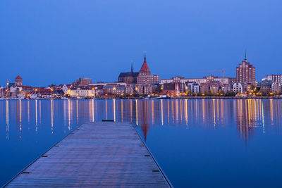 Illuminated cityscape by sea against clear blue sky at night