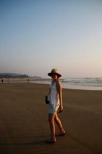 Full length of woman standing at beach against clear sky during sunset