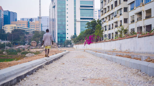 Rear view of man walking on road amidst buildings