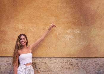 Portrait of smiling young woman standing against wall