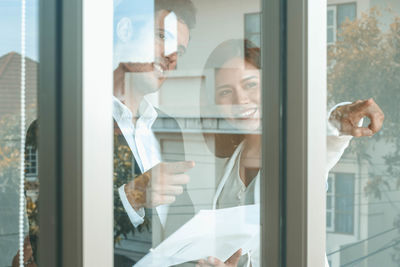 Smiling friends looking through window of house