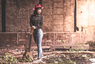 Woman with guitar standing against wall