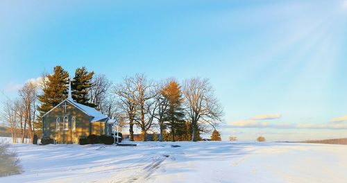 Trees surround church on snow covered ground against clear sky