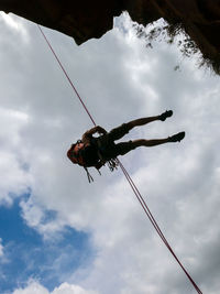 Low angle view of man hanging on rope against sky