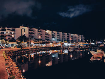 Illuminated buildings by river against sky at night