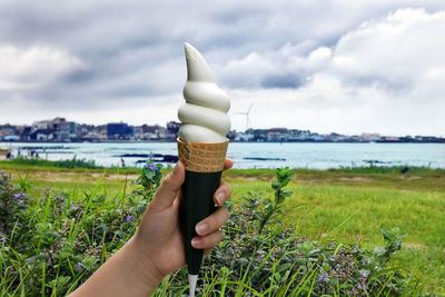 Midsection of person holding icecream on field against sky