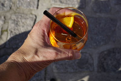 Cropped image of hand holding aperol spritz on footpath