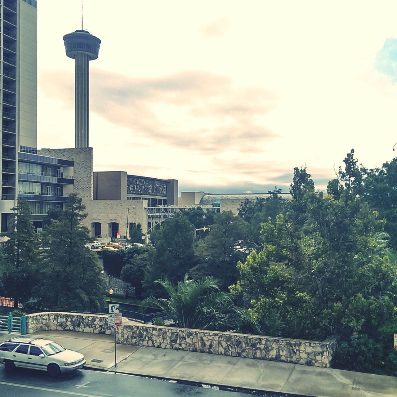 building exterior, architecture, built structure, tree, sky, transportation, city, mode of transport, cloud - sky, street light, car, land vehicle, cloudy, growth, street, outdoors, water, tall - high, cloud, incidental people