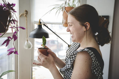 Young woman smiles and laughs at one of her plants in a bright room