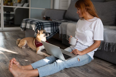 Rear view of woman and dog using laptop