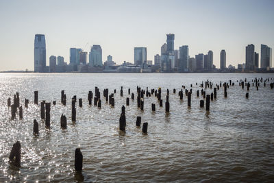 Wooden posts in sea against modern buildings in new york city