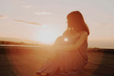 Mature woman sitting on terrace against sky during sunset