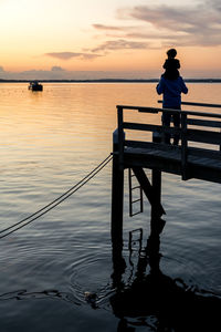 Man standing on pier over sea against sky during sunset