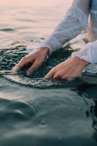 Midsection of woman sitting in sea at sunset