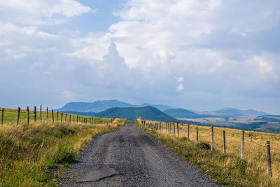 Dirt road amidst field against sky