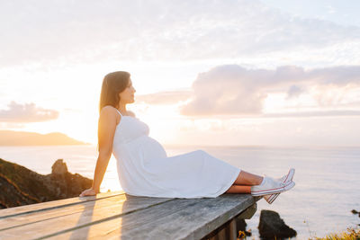 Woman sitting on beach looking at sea against sky