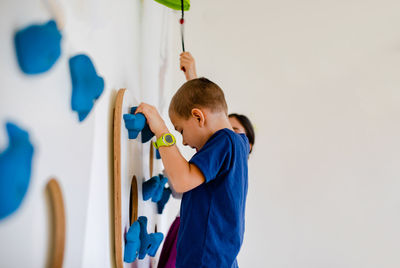 Side view of boy holding multi colored standing against wall