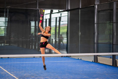 Woman playing padel in a blue grass padel court indoor - sporty woman padel player hitting ball 