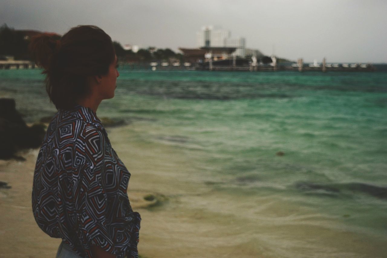 one person, real people, leisure activity, standing, casual clothing, lifestyles, focus on foreground, side view, land, water, sea, three quarter length, nature, day, beach, women, adult, young adult, outdoors, hairstyle, looking at view, profile view, contemplation