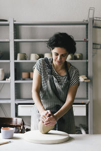 Mature female owner kneading clay in ceramics store