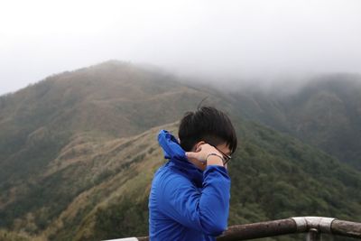Side view of man wearing warm clothing against mountains during foggy weather